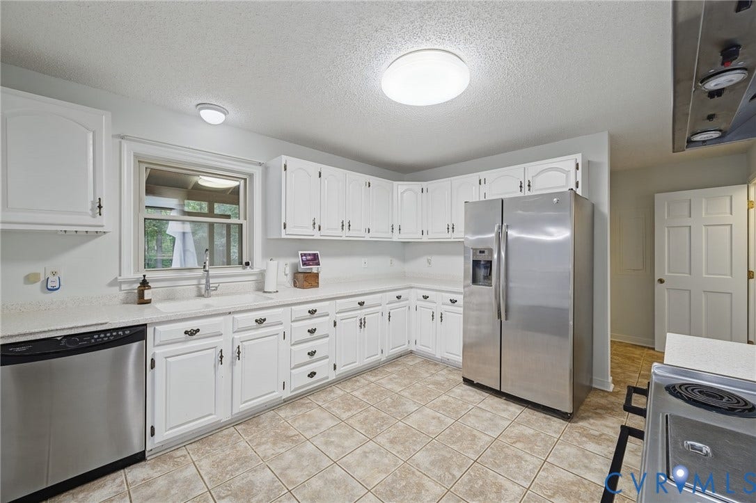 Kitchen featuring white cabinetry, solid-surface countertops, stainless steel appliances, and ceramic tile flooring