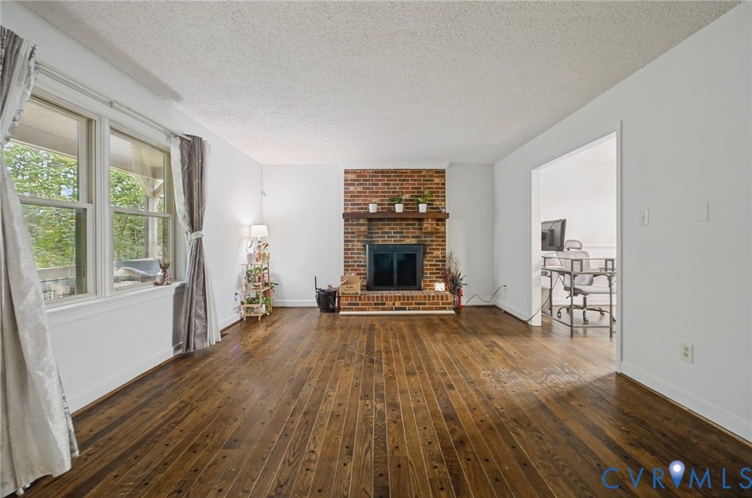 Living area featuring wood-finish flooring, brick fireplace with a wood mantel, and large windows with natural light