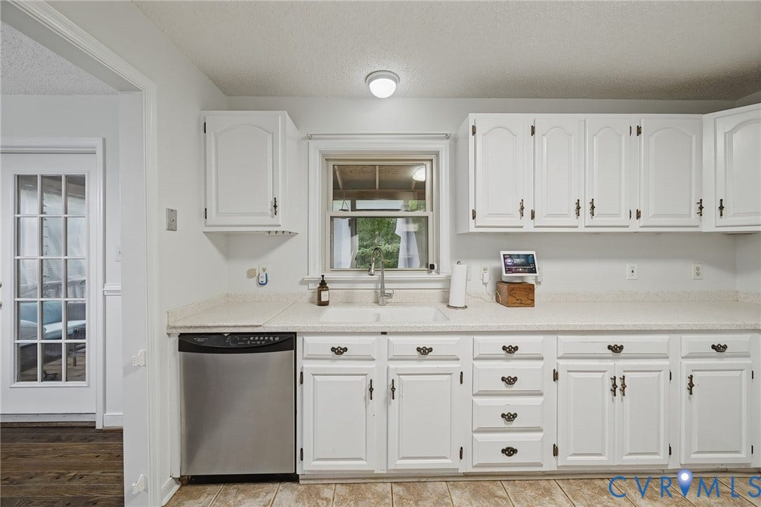 Kitchen featuring white raised-panel cabinetry, neutral solid-surface countertops, integrated dual-basin sink with a gooseneck faucet, stainless steel dishwasher, and tile flooring
