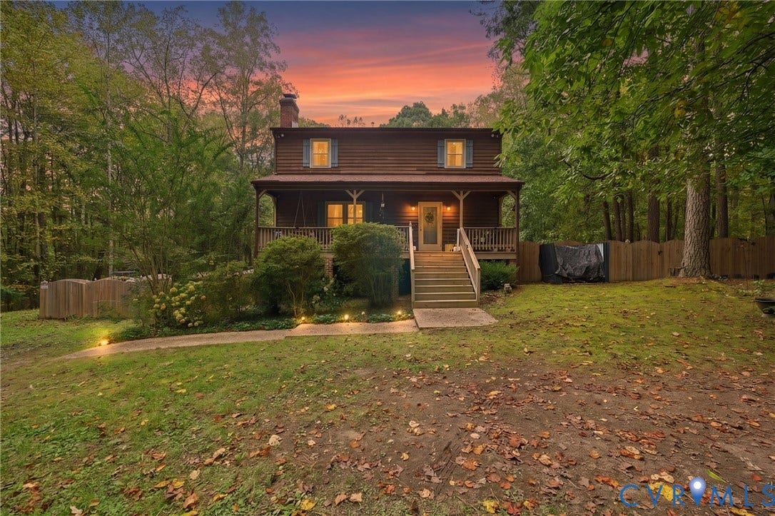 Two-story log exterior residence featuring a covered front porch, wood-slat railings, a chimney, and a fenced backyard