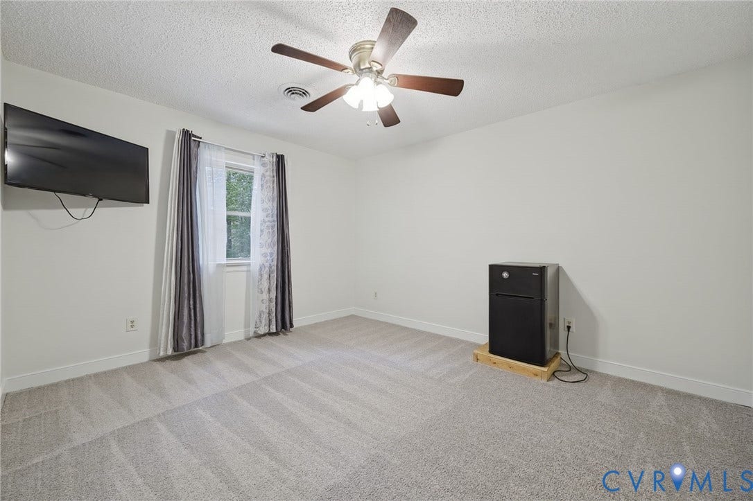 Neutral-toned wall paint, plush carpeting, multi-blade ceiling fan with integrated lighting, and a single-hung window