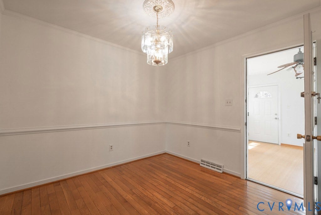 Hardwood-finish flooring, crown molding, chair rail detailing, recessed floor vent, and a crystal chandelier