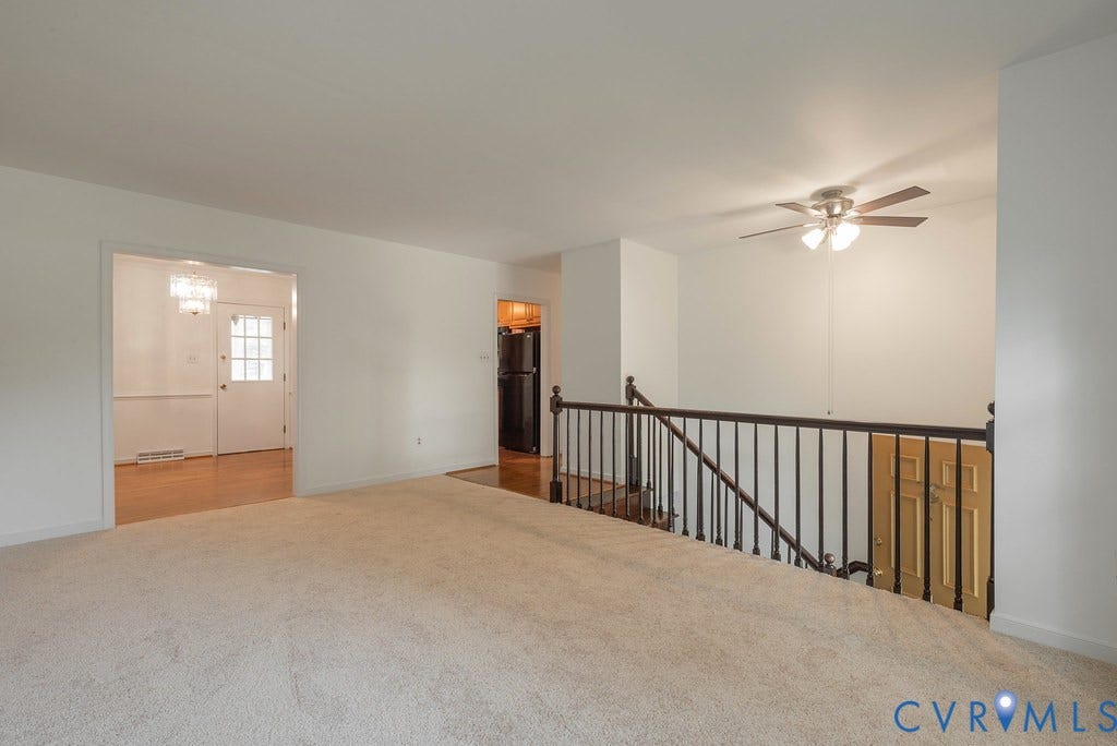 Open concept upper level featuring carpeting, a ceiling fan, and black metal railings