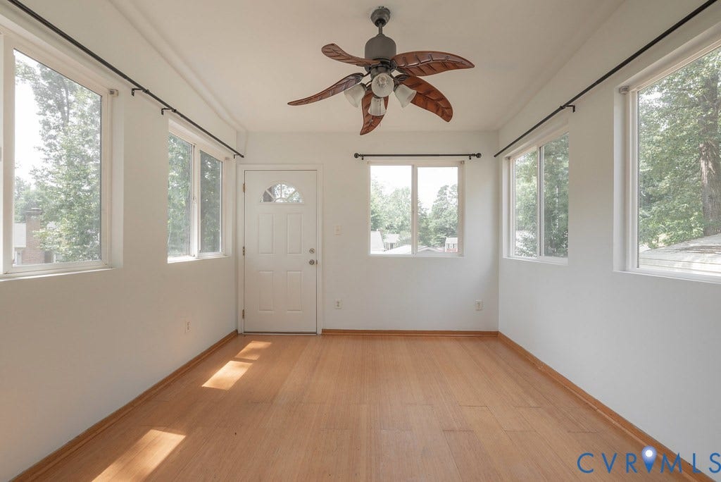 Wood-finish flooring, multiple windows, a white entry door with an arched glass panel, and a ceiling fan with light fixture