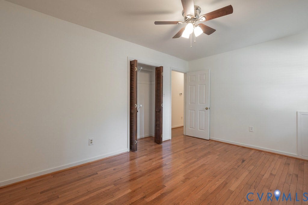 Wood-finish flooring, ceiling fan with integrated lighting, paneled interior door, and louvered bifold closet doors