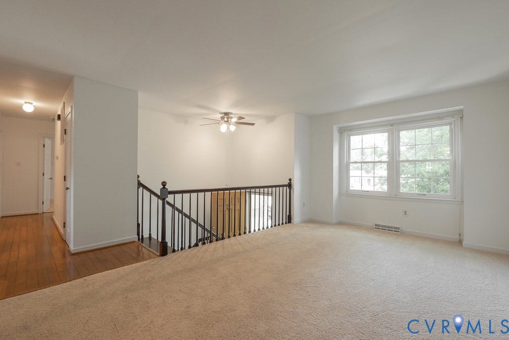 Carpeted living area with a ceiling fan and natural light from a large window