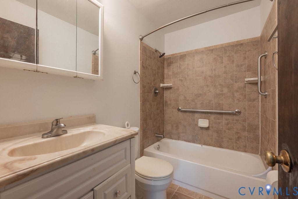 Bathroom featuring a single vanity with an integrated sink, medicine cabinet, and a tiled shower/tub combination with grab bars