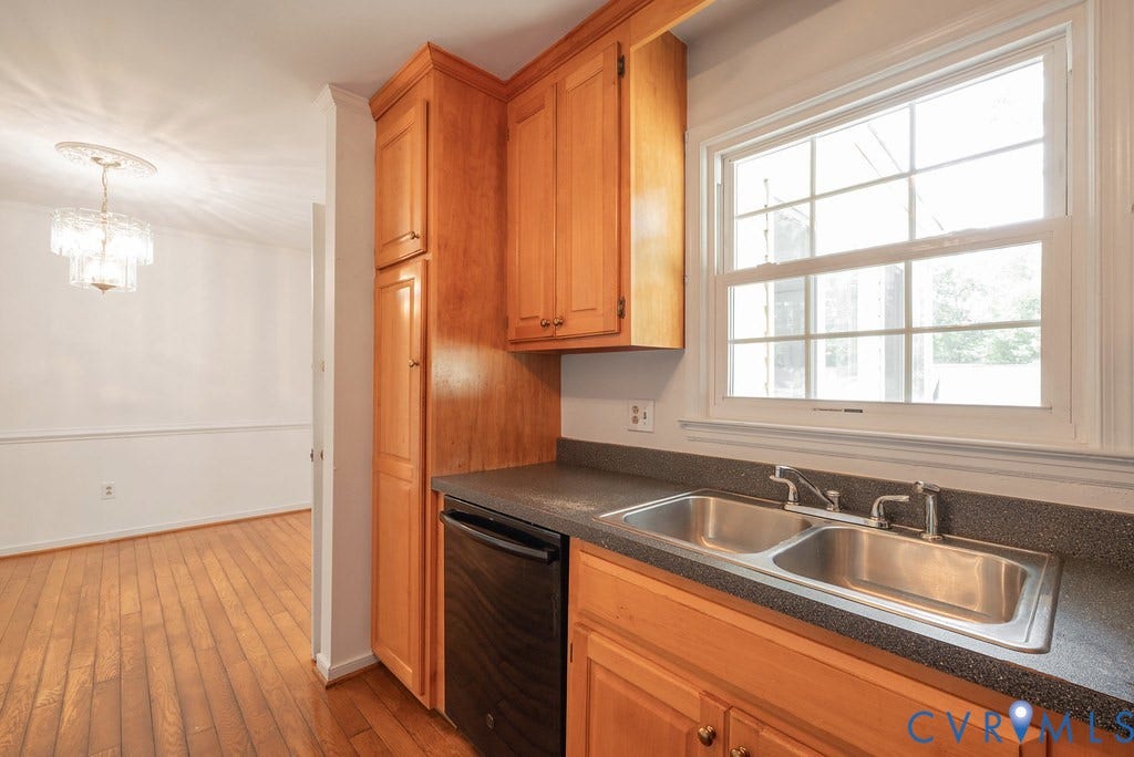 Wood-finish flooring, two-compartment stainless steel sink, wood cabinetry, and a crystal chandelier