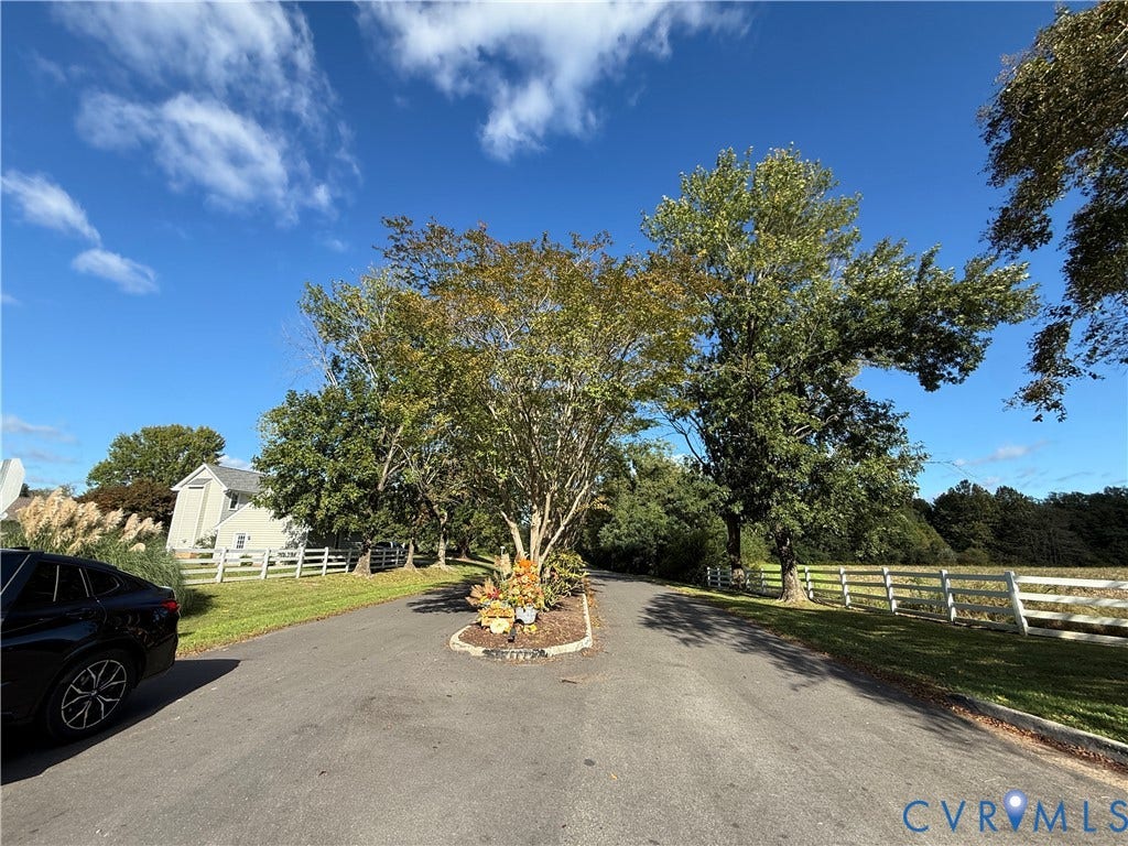 #30 Molly's Way, Urbanna, VA 23175 Paved driveway with a central landscaped island, white fencing, and mature trees