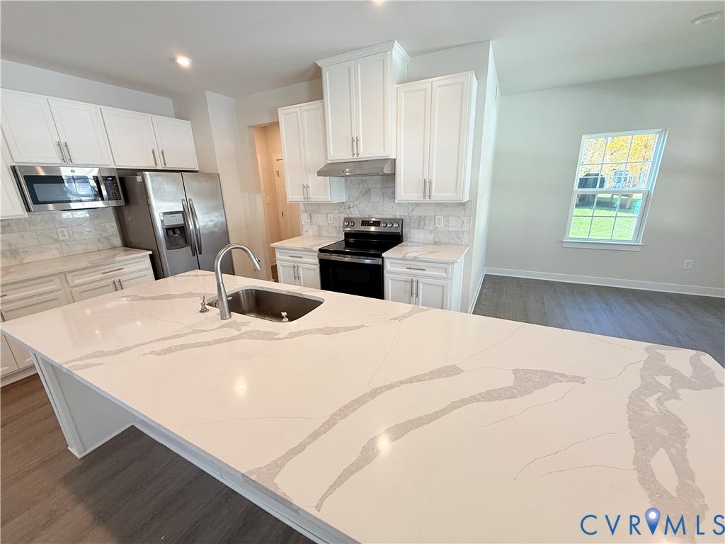 14225 Botsford Avenue, Wellspring, Chester, VA 23831 Kitchen featuring white shaker-style cabinetry, a large central island with a solid surface countertop, stainless steel appliances, stone-look tile backsplash, and wood-finish flooring