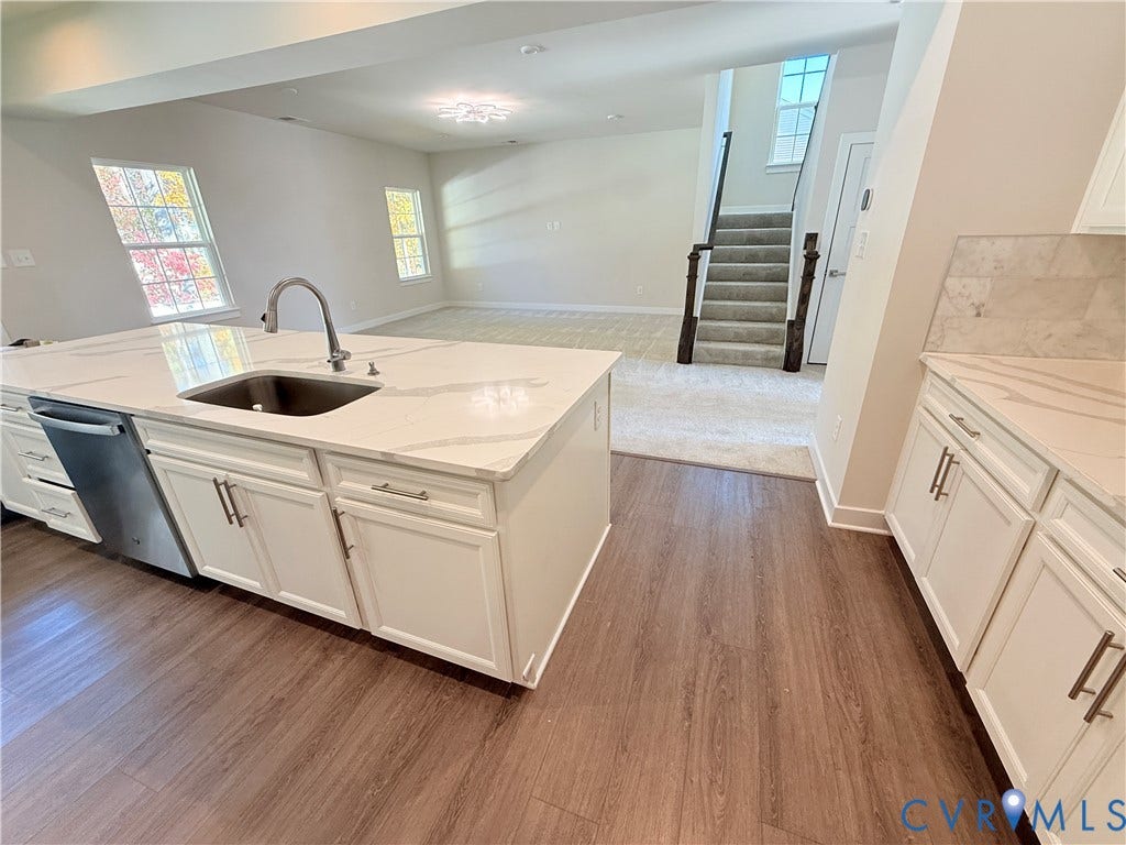 14225 Botsford Avenue, Wellspring, Chester, VA 23831 Kitchen featuring a center island with a stone-finish countertop and an under-mount sink, white cabinetry with silver-tone hardware, wood-finish flooring, and a stone-finish tile backsplash