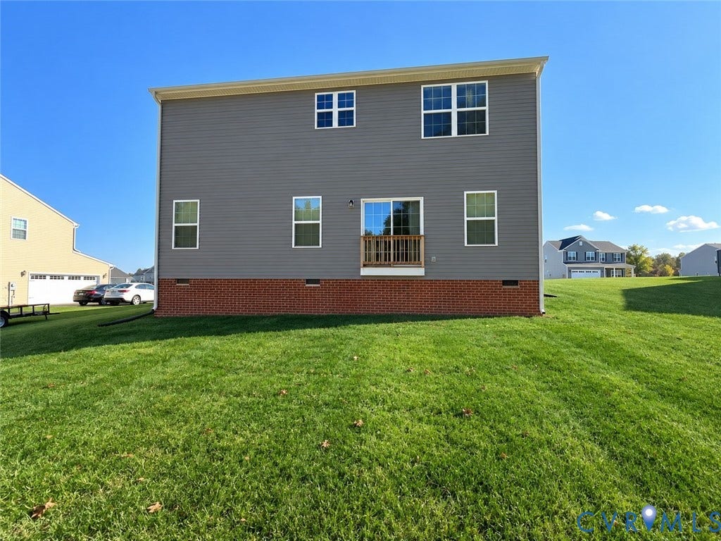 14225 Botsford Avenue, Wellspring, Chester, VA 23831 Rear exterior featuring gray horizontal siding, red brick foundation, sliding glass door with a wood railing, and an expansive grass lawn