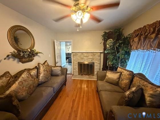 Hardwood flooring, ceiling fan with light fixture, fireplace with stone surround, window with valance and sheer curtain, white paneled doors
