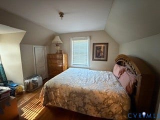 Bright upper-level bedroom featuring sloped ceilings, wood-finish flooring, and abundant natural light from a multi-pane window