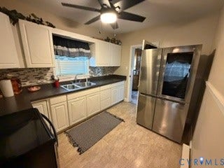 Galley-style kitchen featuring white cabinetry, dark countertops, stainless steel appliances including a French-door refrigerator, and a tile backsplash