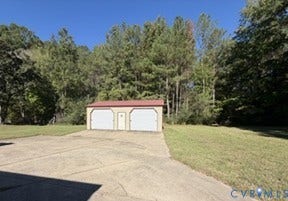 Detached two-car garage with white garage doors and a red roof, concrete drive, and surrounding mature trees