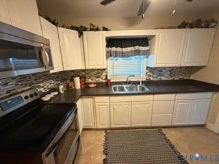 White cabinetry, stainless steel microwave, stainless steel range, dark countertops, and a tile backsplash