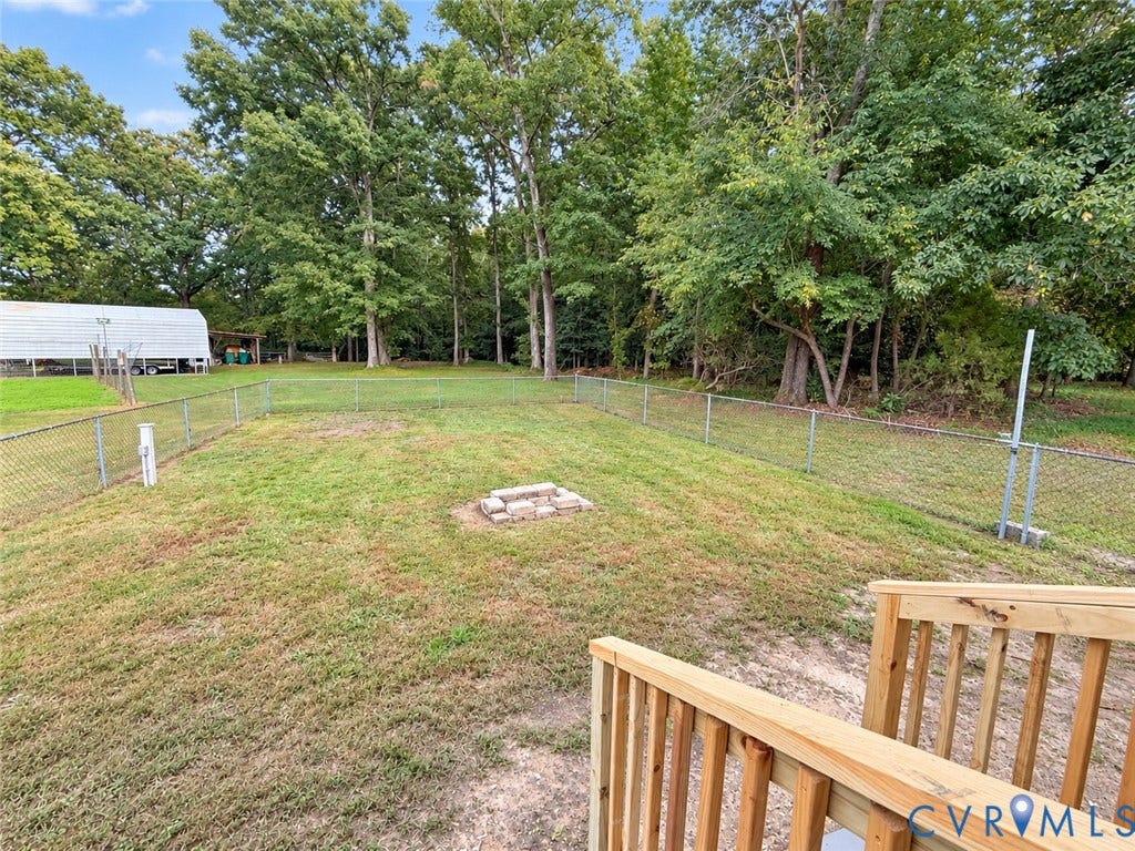 Expansive yard featuring a chain-link fence, a stone fire pit, and mature trees