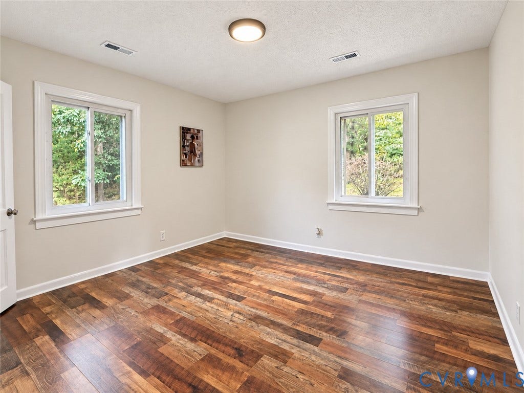 Wood-finish flooring with white trim, two windows, and a flush mount ceiling light