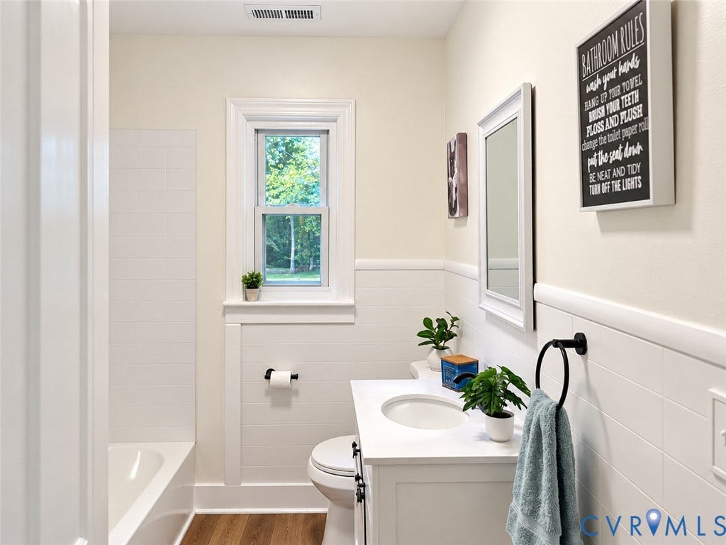 White subway tile shower surround, wood-finish flooring, white vanity with integrated sink, framed mirror, and a single-hung window