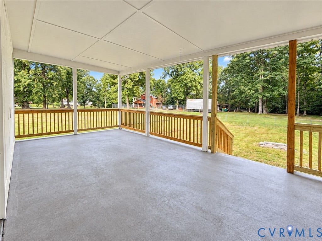 Covered porch featuring a concrete surface, wood railing, and white support columns