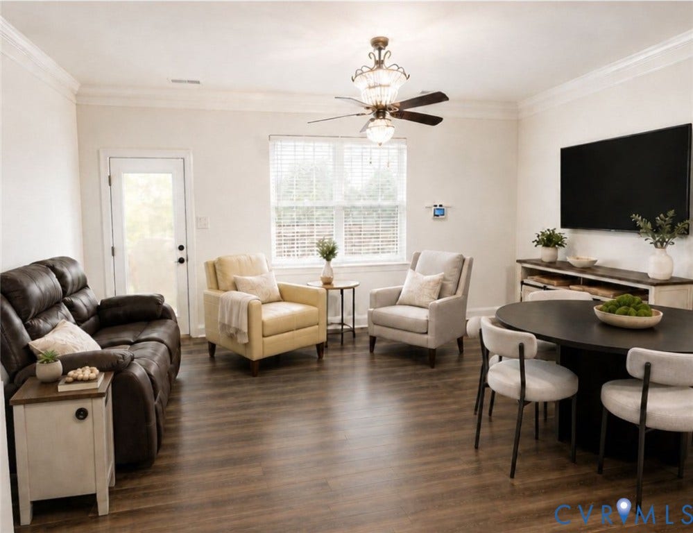 6722 Gibe Lane, Chesterfield, VA 23234 Open-concept room featuring wood-finish flooring, crown molding, double-hung windows with blinds, and a central chandelier ceiling fan. This image has been digitally enhanced using AI for lighting and clarity.