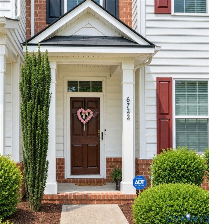 6722 Gibe Lane, Chesterfield, VA 23234 Siding exterior with brick accents, covered entry with gable roof, dark wood-finish front door with transom window, and red shutters. This image has been digitally enhanced using AI for lighting and clarity.