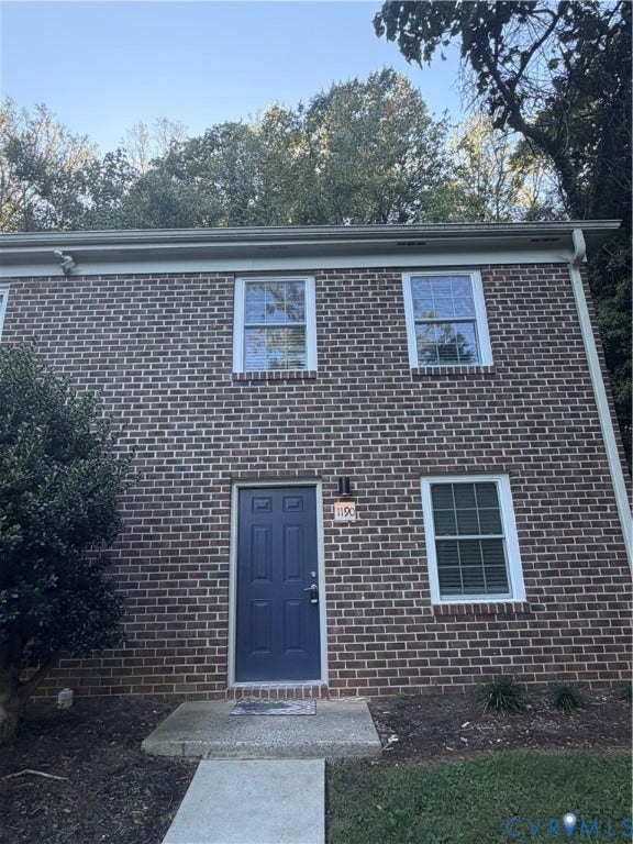 Brick facade featuring a panel door, white window frames, and a concrete walkway