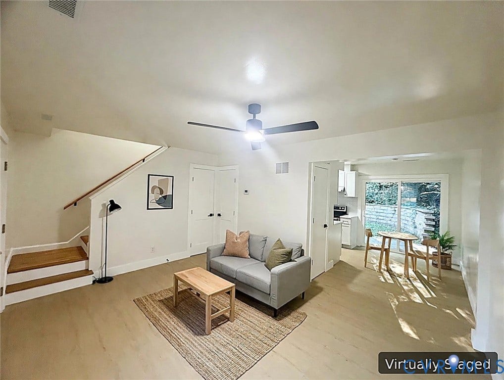 Wood-finish flooring throughout, featuring a modern ceiling fan, staircase with wood handrail, and white double-panel doors