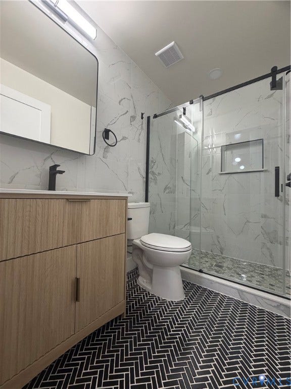 Bathroom featuring black herringbone tile flooring, a wood-finish vanity with a single sink, a sliding glass shower enclosure, a built-in shower niche, and white marble-look wall tile