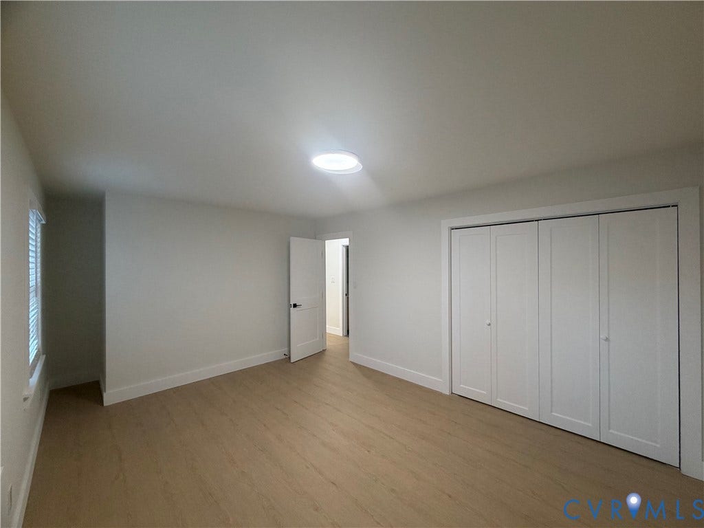 Light wood-finish flooring, white walls, built-in closet with bi-fold doors, white interior door, and a flush-mount ceiling light