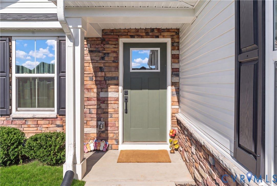 7580 Southamptonshire Way, Autumn Pines, New Kent, VA 23124 Front entry with a sage green door, stone veneer detailing, white siding, and dark shutters
