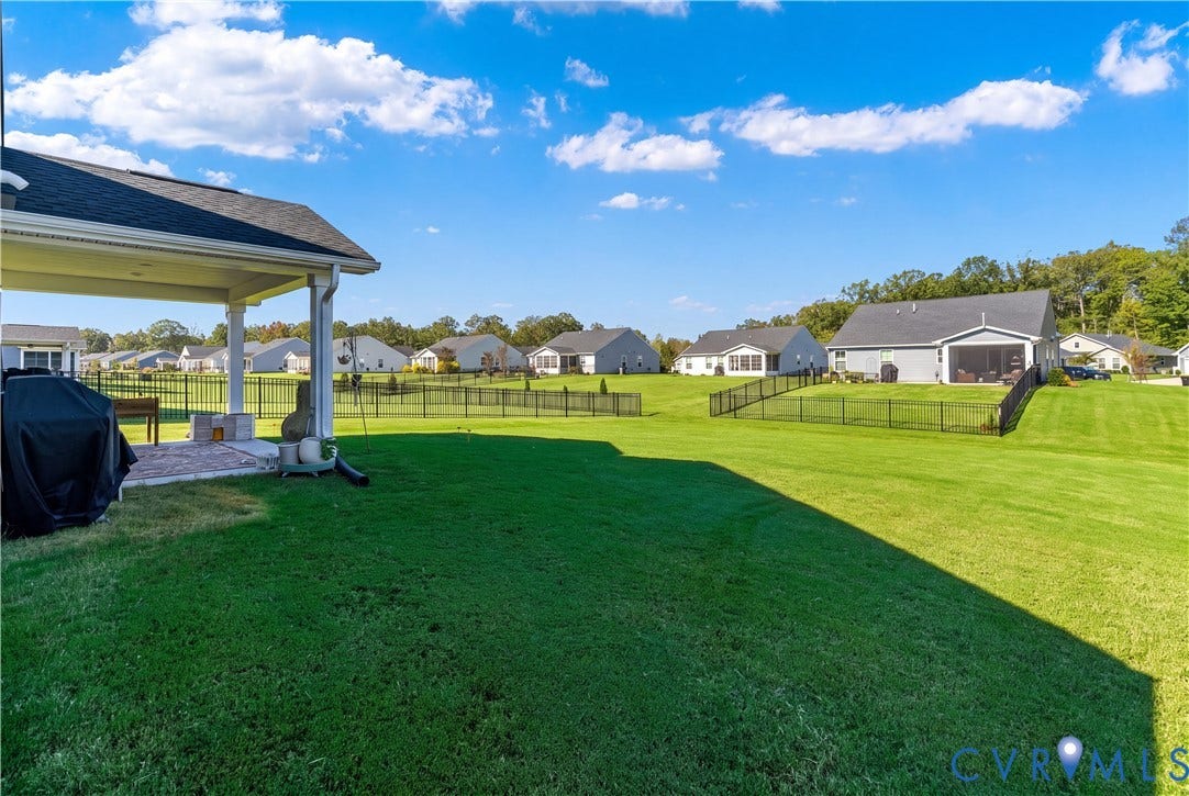 7580 Southamptonshire Way, Autumn Pines, New Kent, VA 23124 Expansive green lawn with a covered patio, black metal fencing, and visible built-in stone fire feature
