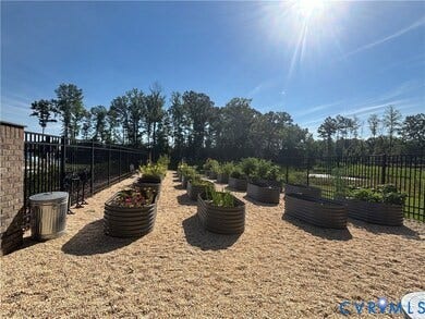 7580 Southamptonshire Way, Autumn Pines, New Kent, VA 23124 Garden area featuring multiple raised garden beds, a gravel-covered ground surface, and a black metal fence