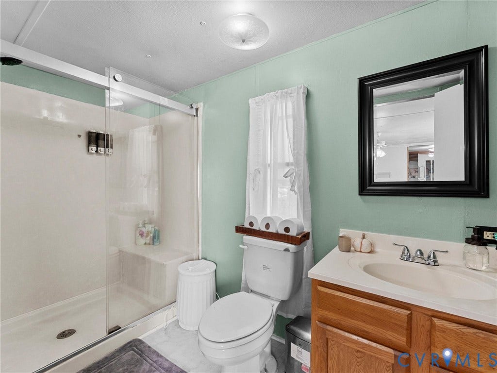 17009 Lansmill Drive, South Chesterfield, VA 23834 Walk-in shower with sliding glass door, built-in shower bench, single vanity with wood-finish cabinetry, and framed mirror