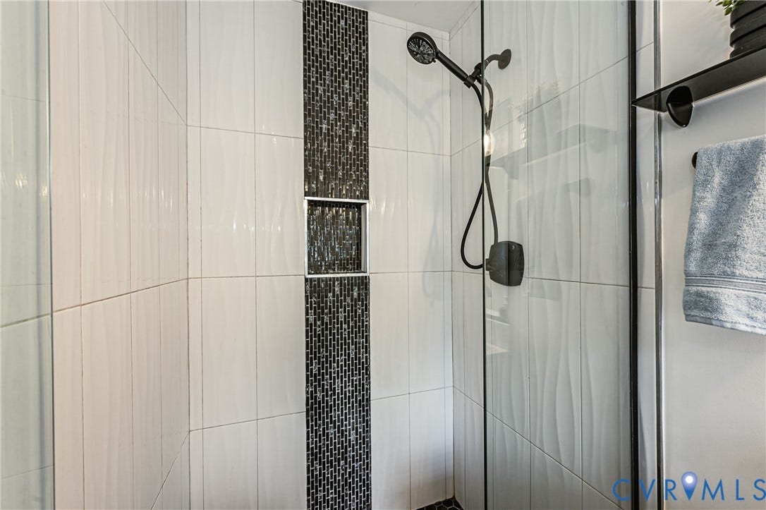 1608 Lochwood Drive, Henrico, VA 23238 Modern bathroom featuring a walk-in shower with frameless glass enclosure, dual showerheads with handheld spray, matte black fixtures, and linear wall tile in white with a decorative mosaic accent stripe