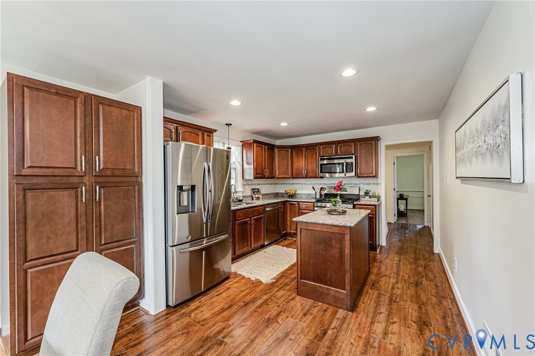 1608 Lochwood Drive, Henrico, VA 23238 Spacious kitchen featuring rich wood cabinetry, stainless steel appliances including a French-door refrigerator, a centered island with seating, wood-finish flooring throughout, and recessed lighting in the ceiling
