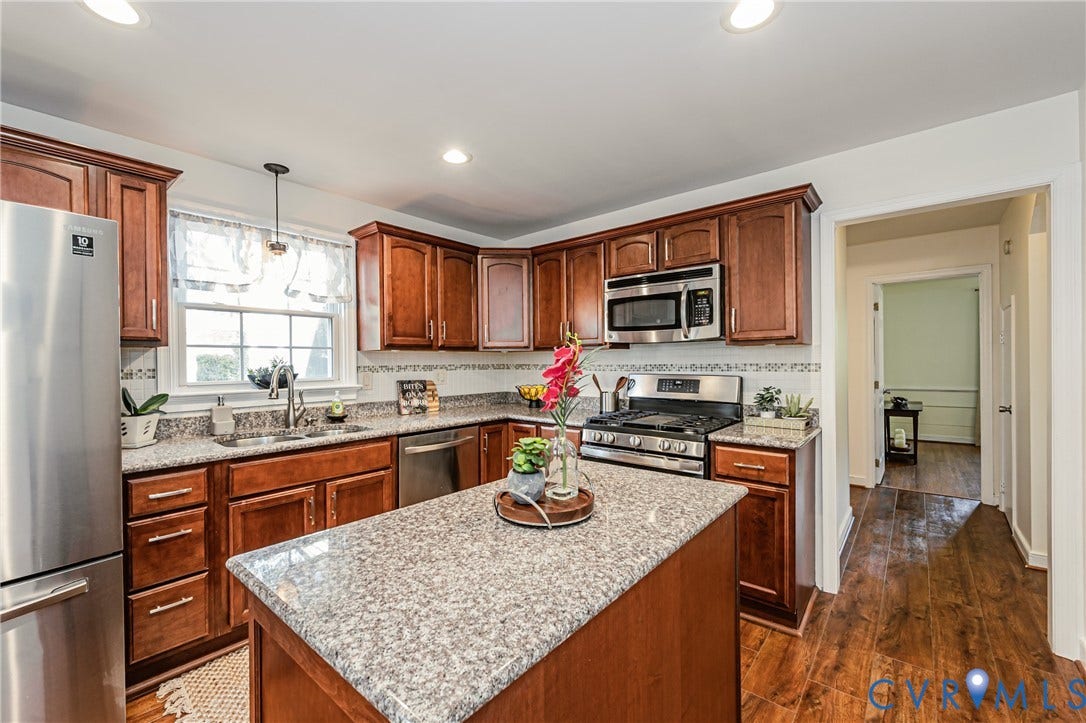 1608 Lochwood Drive, Henrico, VA 23238 Kitchen featuring wood-finish flooring, wood cabinetry, stainless steel appliances, a corner sink with a window, and a central island with a light-toned countertop