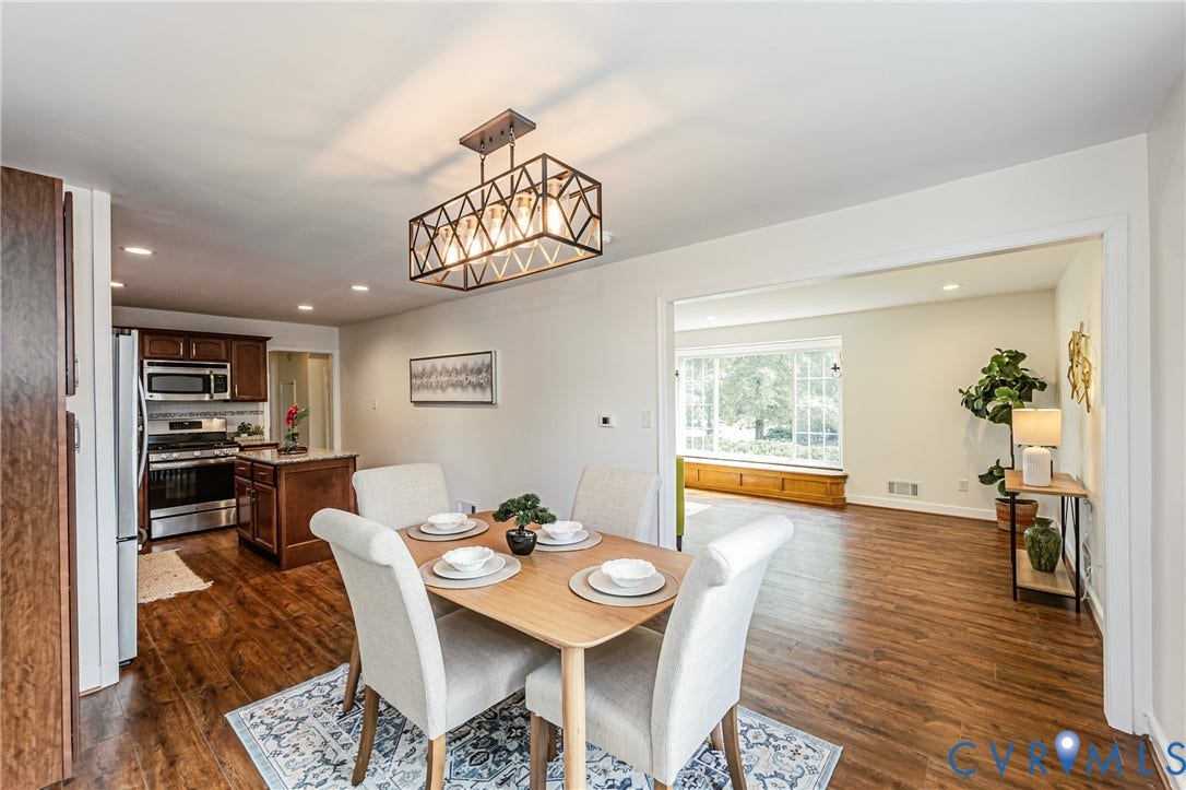 1608 Lochwood Drive, Henrico, VA 23238 Open-concept dining and kitchen area featuring warm wood-finish flooring, a geometric pendant light fixture, white painted cabinetry with stainless steel appliances, and abundant natural light from multiple windows