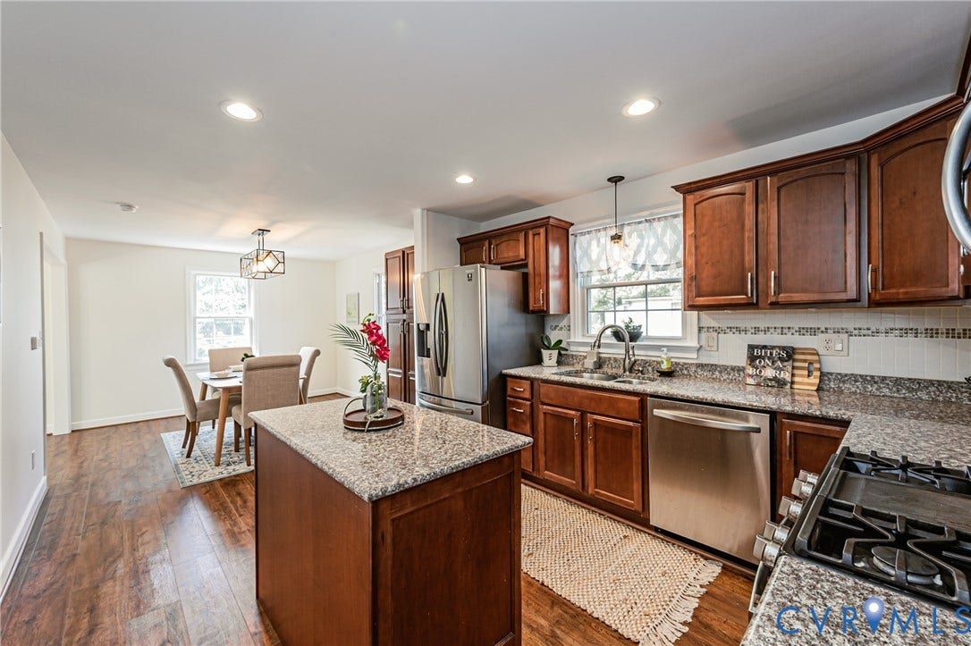 1608 Lochwood Drive, Henrico, VA 23238 Gourmet kitchen featuring rich wood cabinetry, stainless steel appliances, granite countertops with coordinating backsplash, a center island with seating, and hardwood flooring that extends into the adjoining dining and living areas