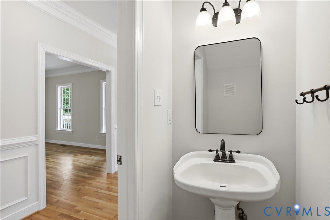 10721 Sheppards Way Drive, Sheppards Way, Glen Allen, VA 23060 Elegant powder room featuring a curved pedestal sink with chrome faucet, framed mirror with matte black trim, and vintage-style sconce lighting