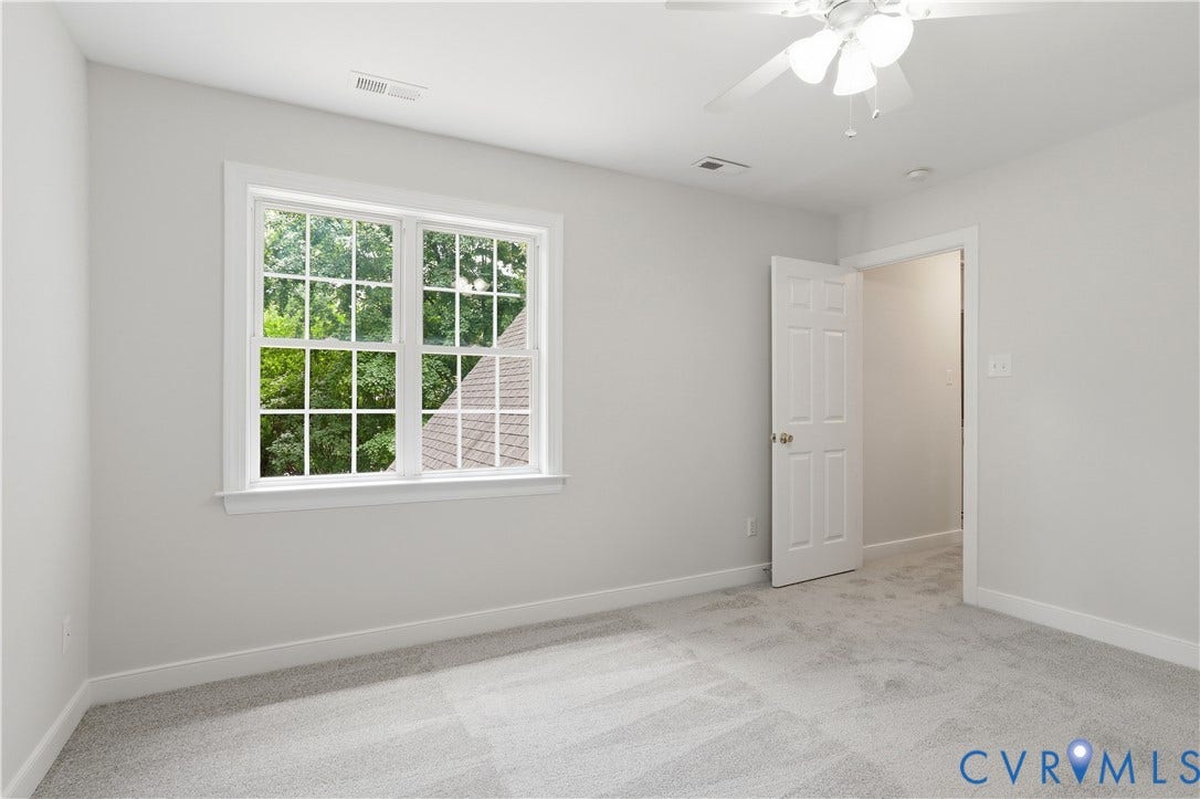 10721 Sheppards Way Drive, Sheppards Way, Glen Allen, VA 23060 Bright, light-filled bedroom with large multi-pane windows framing natural outdoor scenery, neutral wall finishes, neutral-toned carpet flooring, and two white panel doors providing access to additional spaces