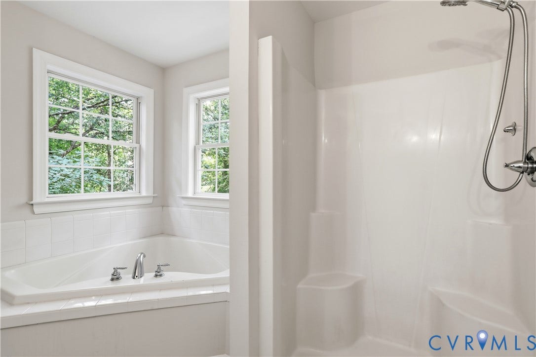 10721 Sheppards Way Drive, Sheppards Way, Glen Allen, VA 23060 Spa-inspired primary bathroom featuring a soaking tub with chrome fixtures, a walk-in shower enclosure with rainfall showerhead, crisp white subway tile surround, and abundant natural light from dual casement windows overlooking mature landscaping