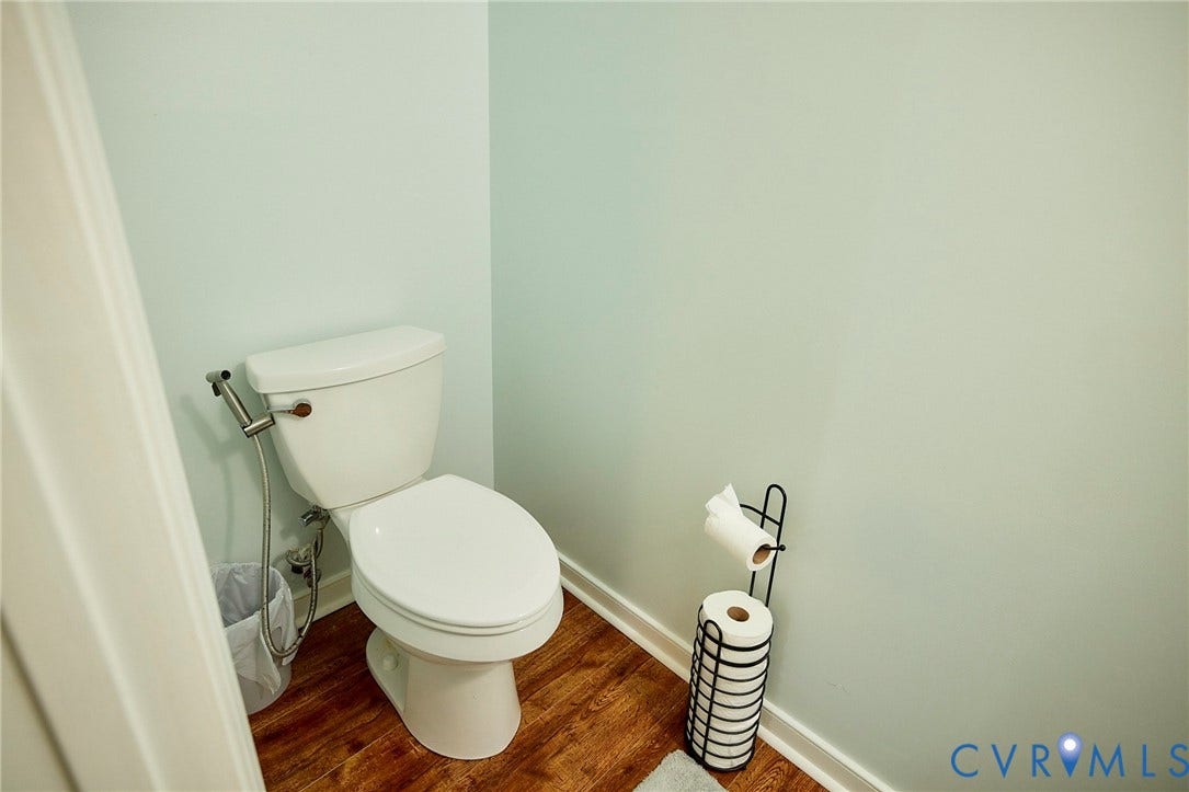 2633 Bradway Lane, Henrico, VA 23233 Compact powder room featuring a white ceramic toilet with soft-close seat, chrome supply lines and shutoff valves, wood-finish flooring, and soft sage-green walls