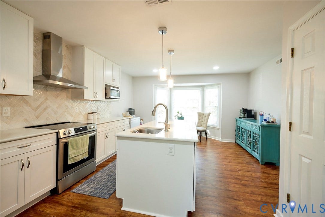 2633 Bradway Lane, Henrico, VA 23233 Kitchen featuring white cabinetry, stainless steel appliances, herringbone tile backsplash, an island with an undermount sink, and wood-finish flooring