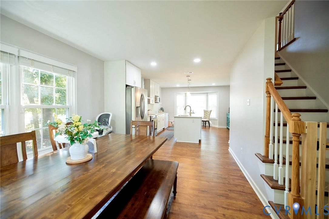2633 Bradway Lane, Henrico, VA 23233 Open-concept dining and kitchen area featuring warm wood-finish flooring throughout, a substantial wood dining table with seating for multiple guests, stainless steel appliances, white cabinetry, and abundant natural light from multiple windows