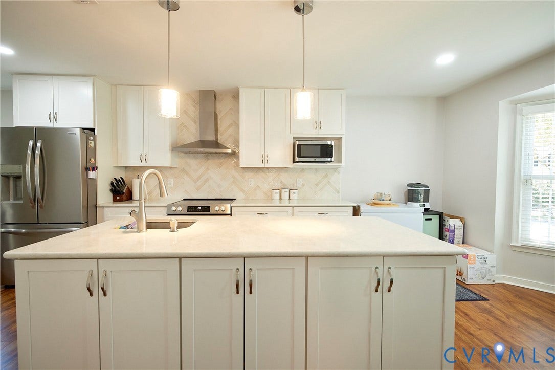 2633 Bradway Lane, Henrico, VA 23233 Modern kitchen featuring a generous island with waterfall-edge countertop, white cabinetry with hardware accents, stainless steel appliances including a range hood, pendant lighting, and wood-finish flooring throughout the open layout