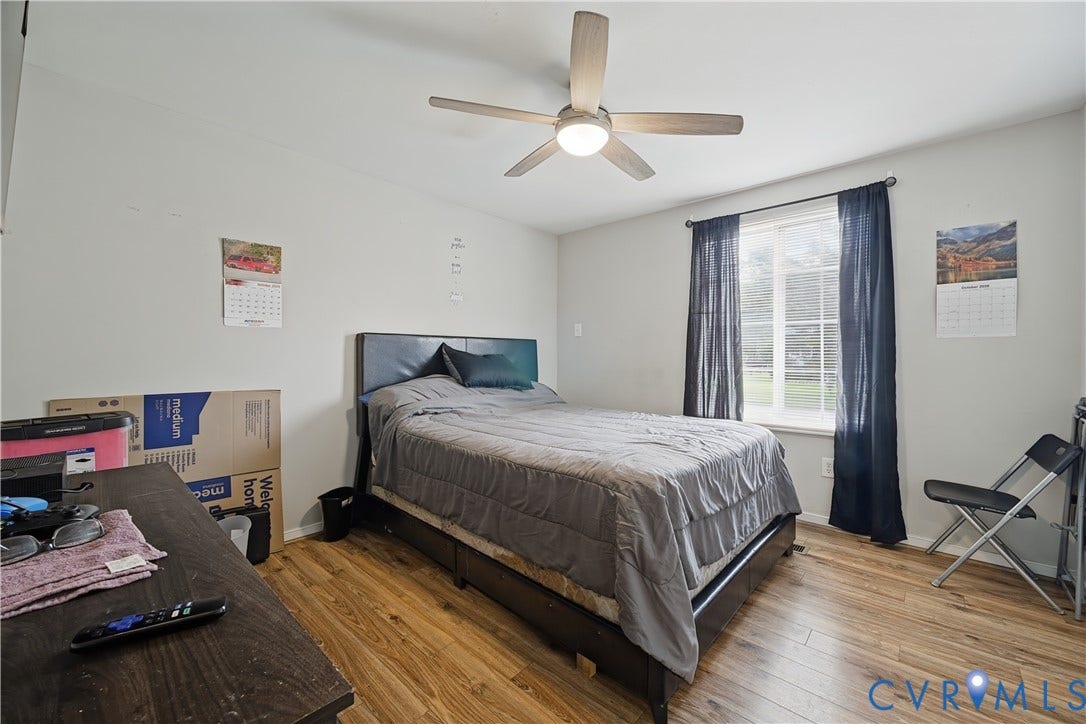 Wood-finish flooring, ceiling fan with integrated lighting, and a window with dark drapery