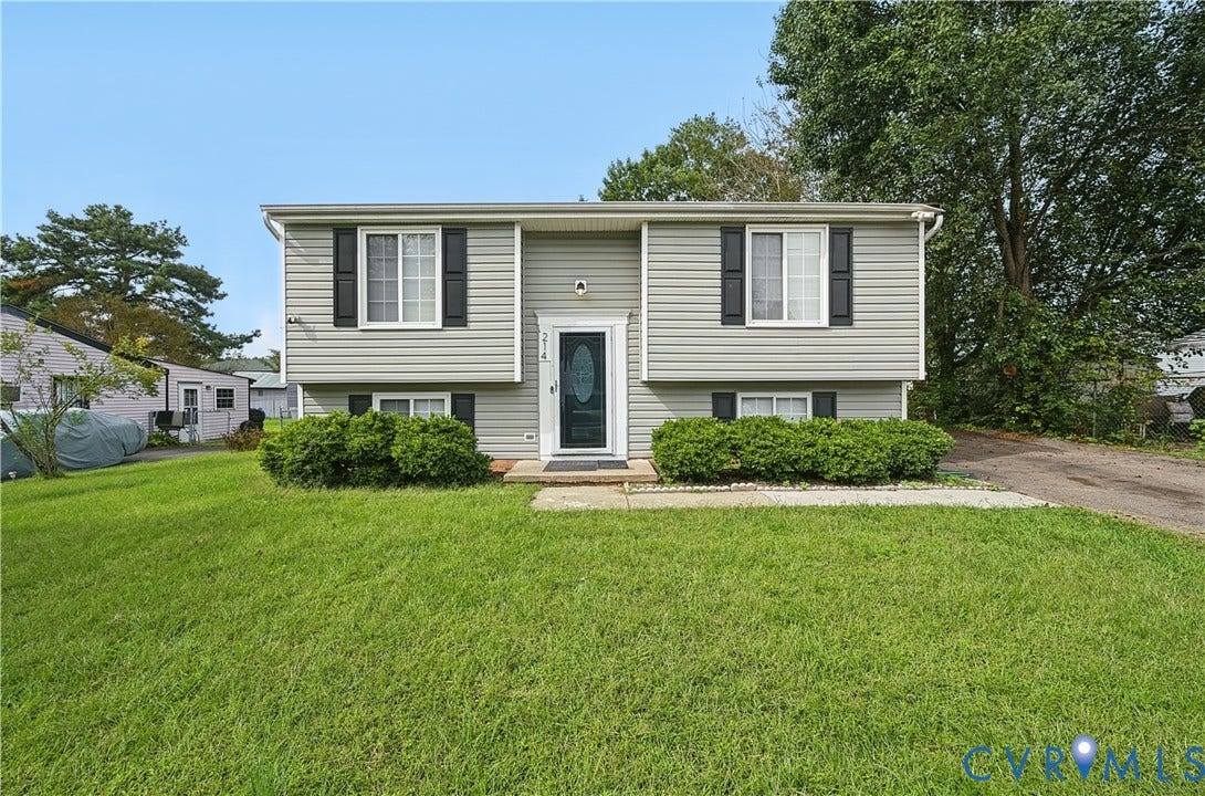 Split-level exterior featuring light gray siding, black window shutters, a front entry with a decorative glass door, and a manicured lawn