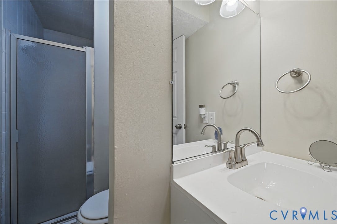 White vanity with integrated sink, brushed nickel faucet, large wall-mounted mirror, and frosted glass shower enclosure